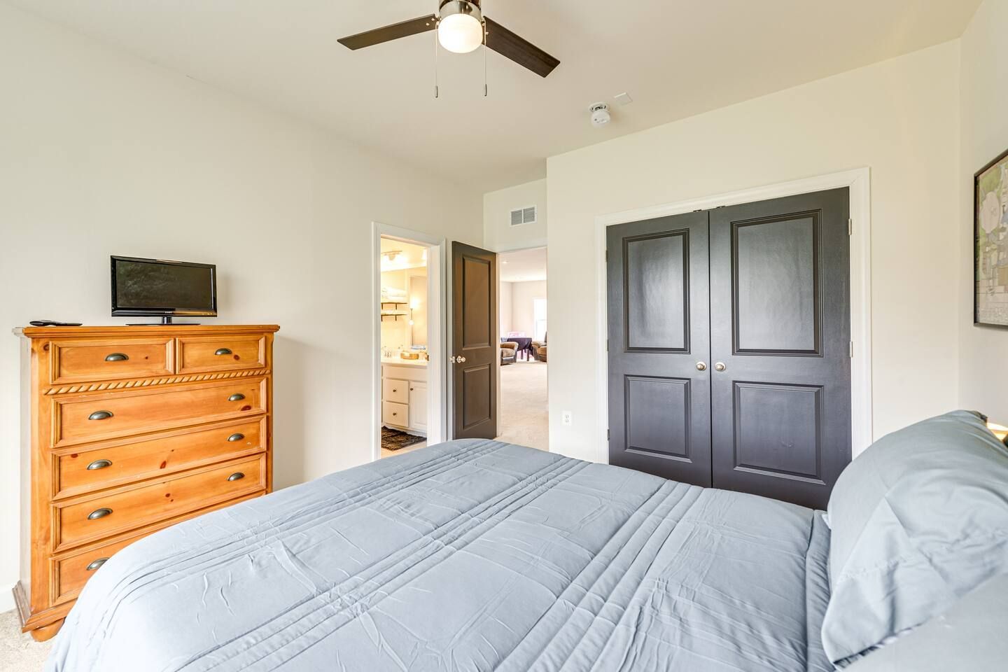 A bedroom with a bed , dresser , television and ceiling fan.