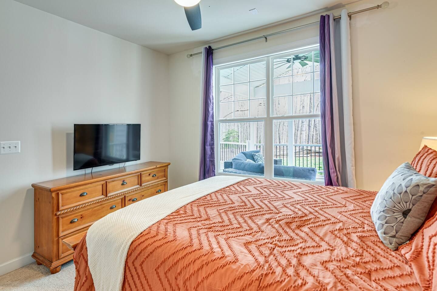 A bedroom with a large bed , dresser , television and sliding glass door.