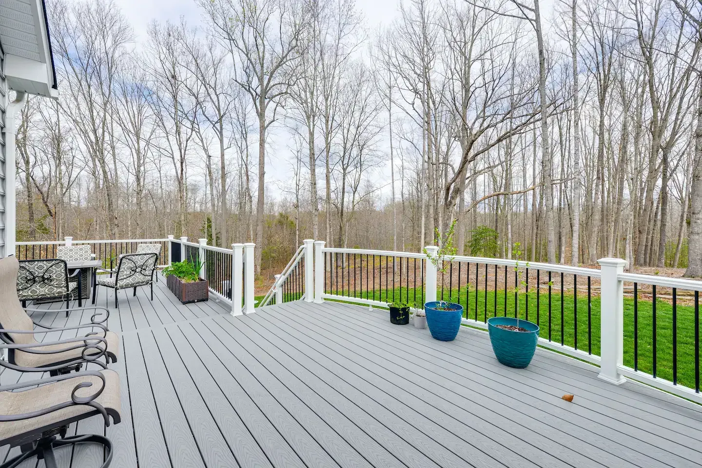 A large gray deck with a white railing and trees in the background.