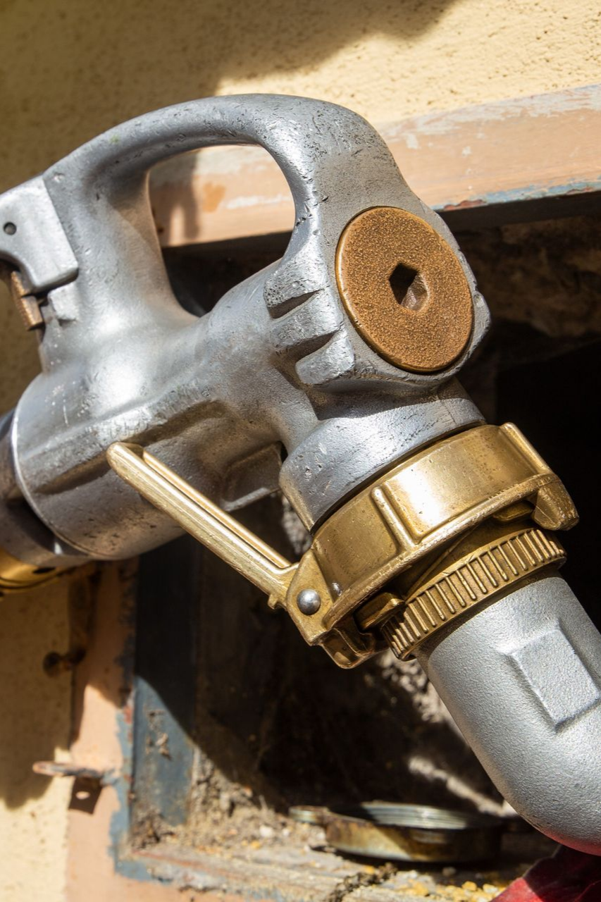Gros plan d'un pistolet à carburant argenté et en laiton, sur fond de mur jaune.