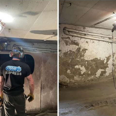 Un homme travaille sur un mur de sous-sol, portant des protections auditives. Mur en béton à la peinture écaillée. Intérieur.