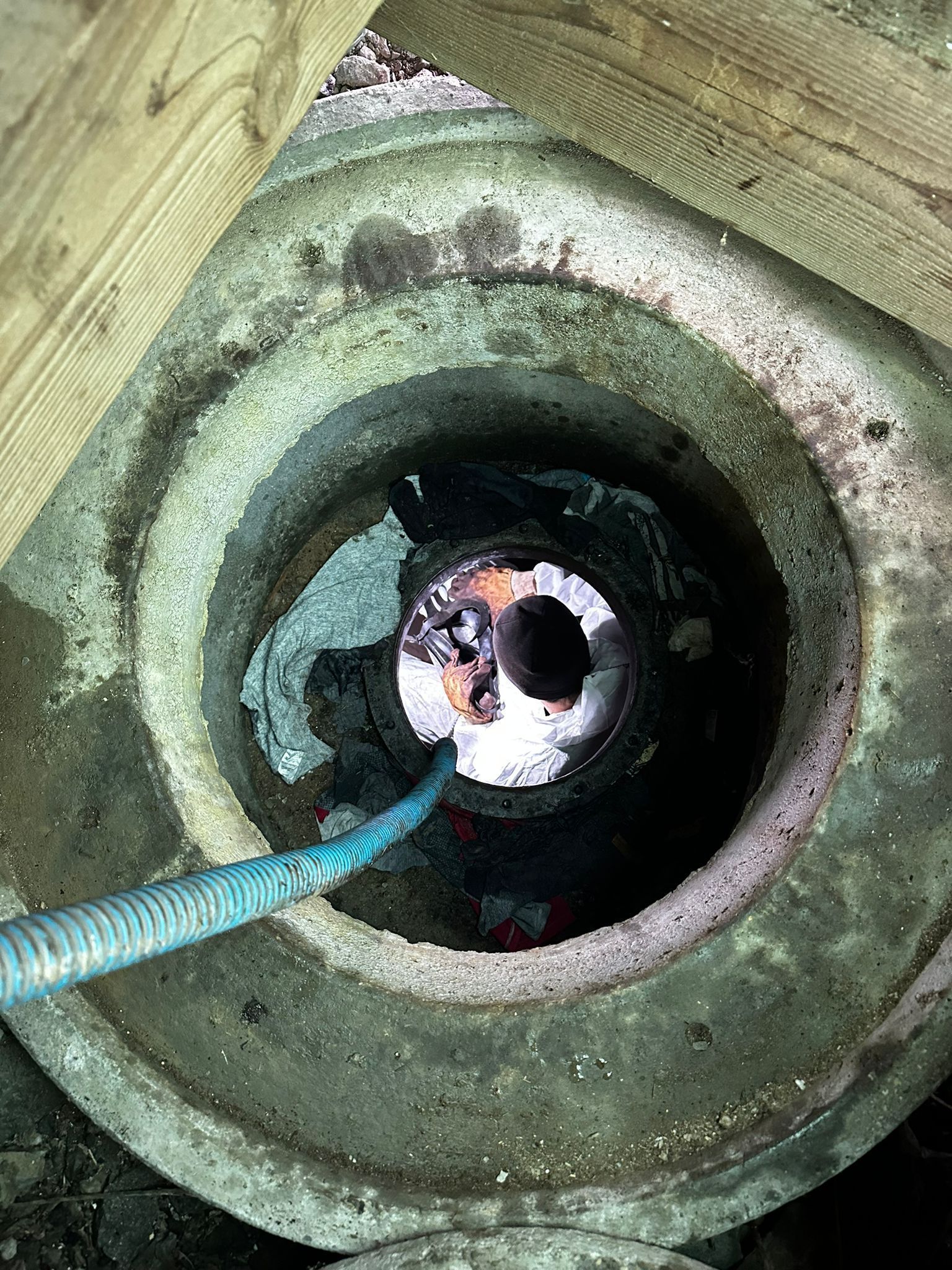 Vue plongeante sur un regard d'accès aux égouts en béton avec un tuyau bleu inséré.
