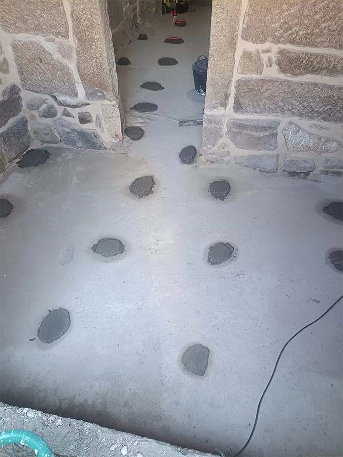 Un suelo de hormigón con agujeros y una pared de piedra al fondo.