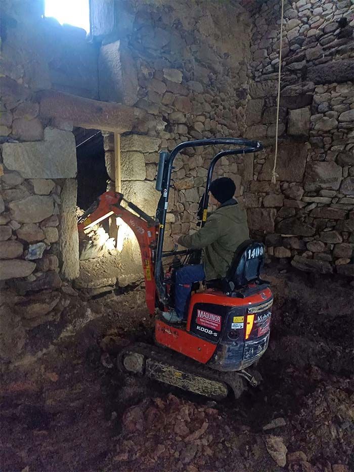 Un hombre conduce una pequeña excavadora en un edificio de piedra.