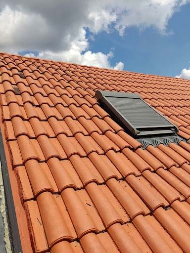 Un techo con tejas rojas y una claraboya sobre él.