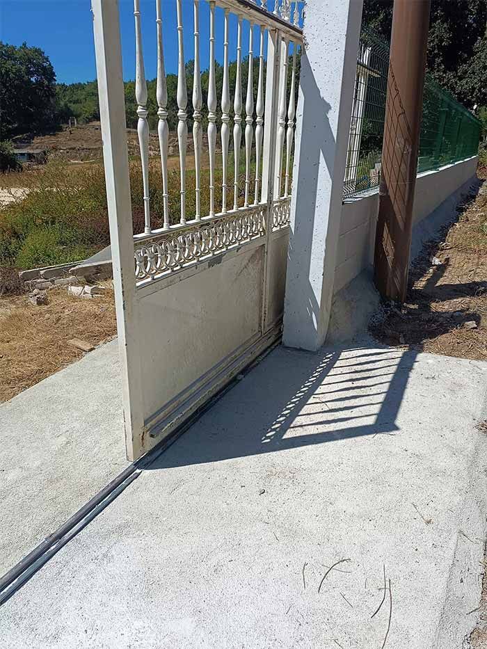 Una puerta blanca con una sombra en el suelo y una valla al fondo.