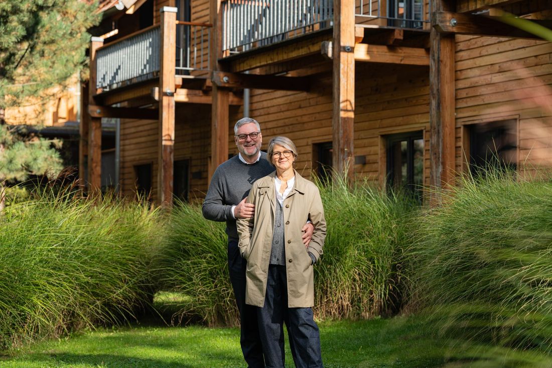 Ein Mann und eine Frau stehen vor einem Holzhaus.