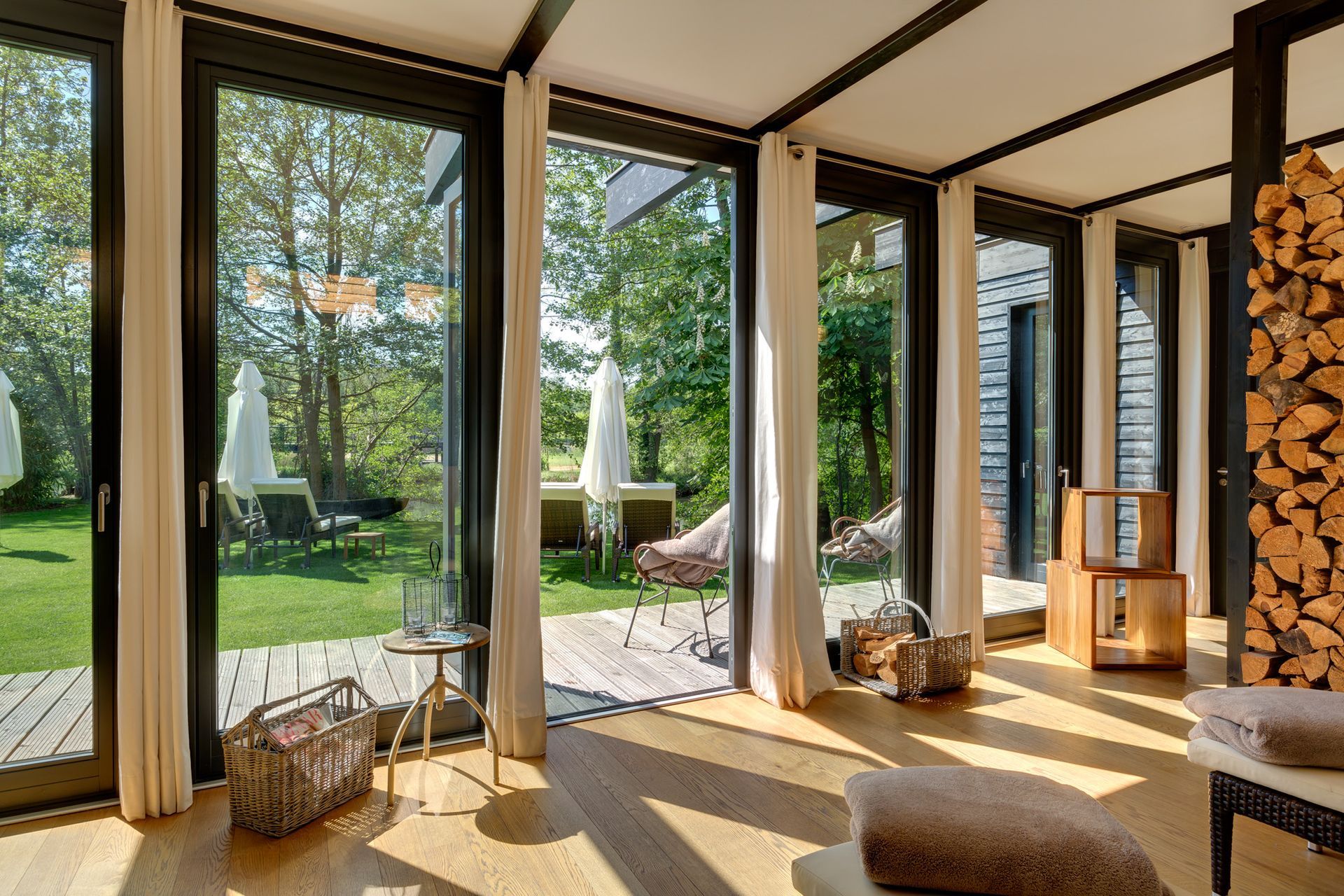 Ein Wohnzimmer mit vielen Fenstern und einem Stapel Holzscheite an der Wand.
