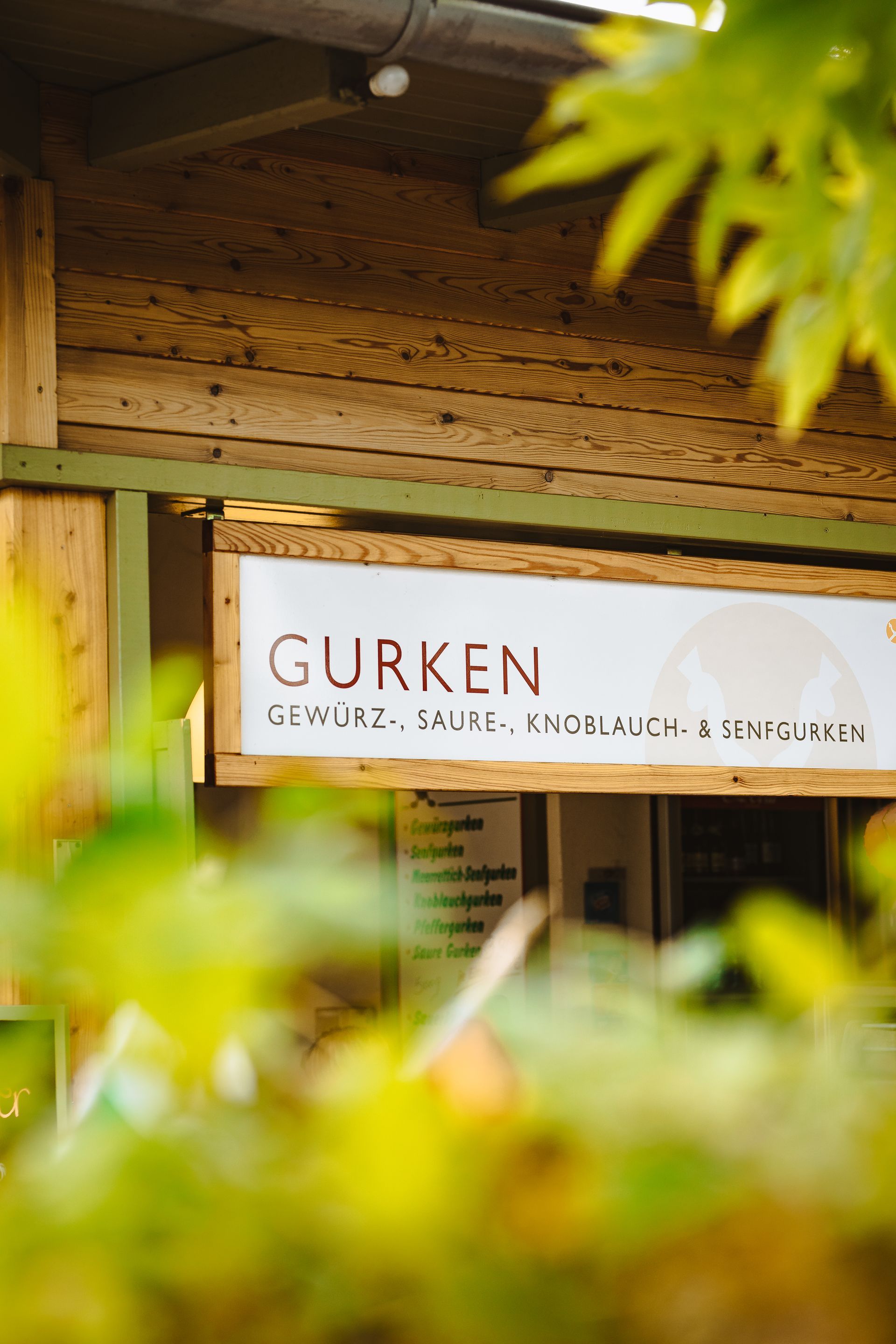 An einer Holzwand hängt ein Schild mit der Aufschrift „Gurken“.