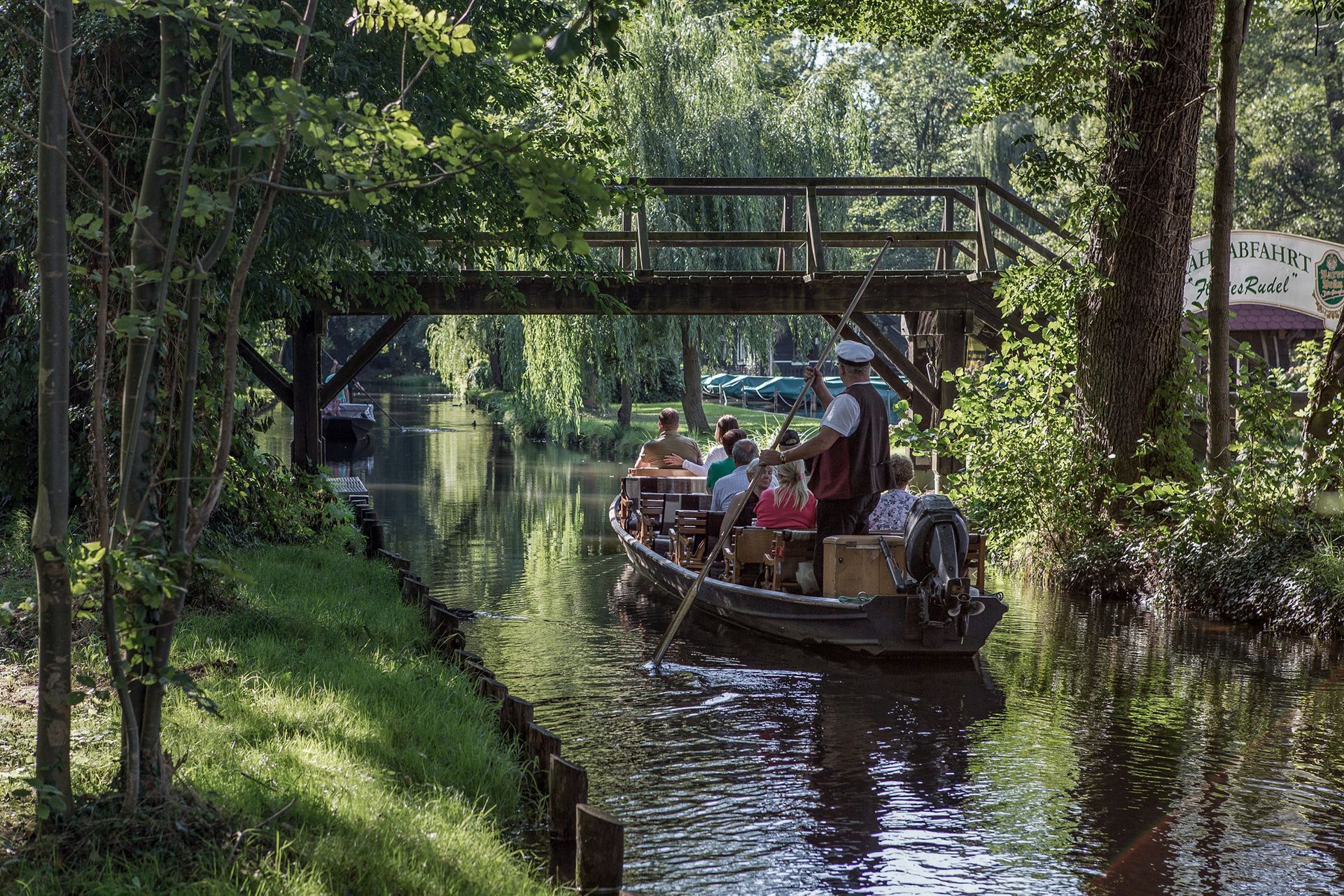 Eine Gruppe von Menschen fährt mit einem Boot einen Fluss hinunter, unter einer Brücke hindurch.