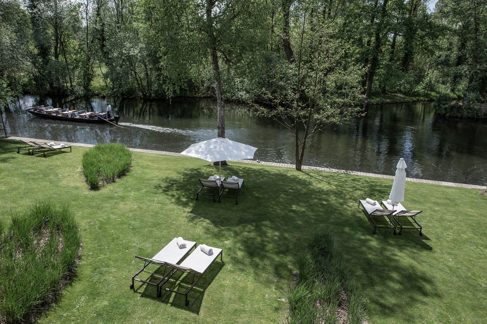 Eine Wiese mit Stühlen und Sonnenschirmen neben einem Fluss.