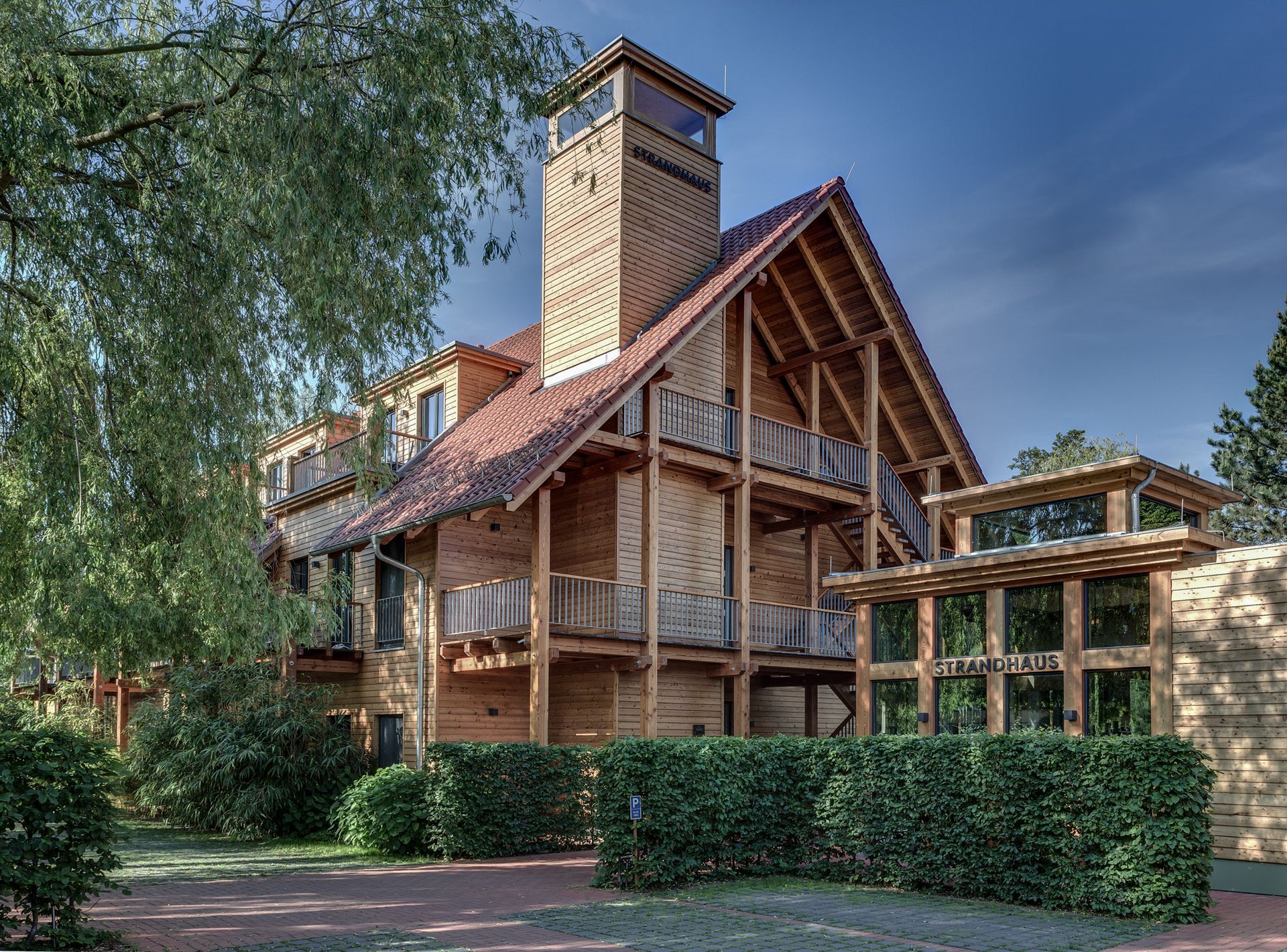 Ein großes Holzhaus mit rotem Dach ist von Bäumen und Büschen umgeben.