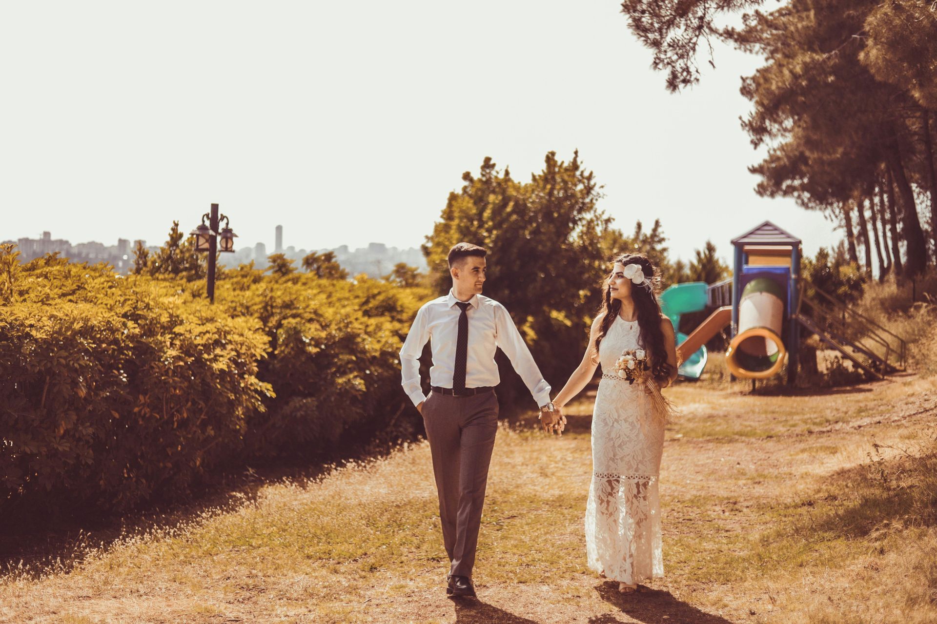 Eine Braut und ein Bräutigam halten Händchen, während sie in einem Park spazieren gehen.