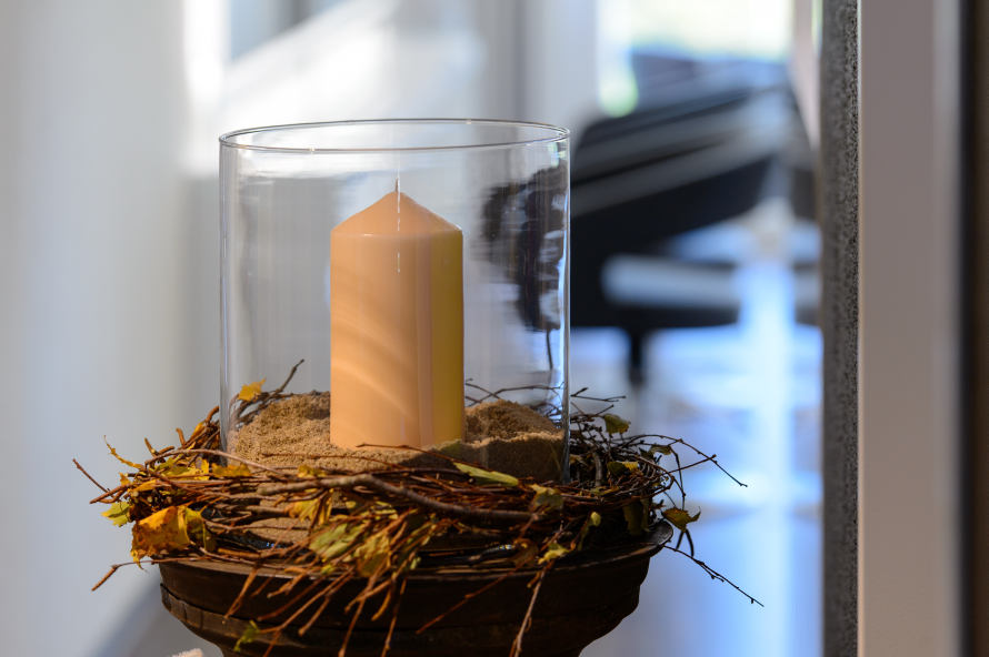Eine Kerze in einem Glas, umgeben von Zweigen und Blättern. Foto von Coiffure Sunshine