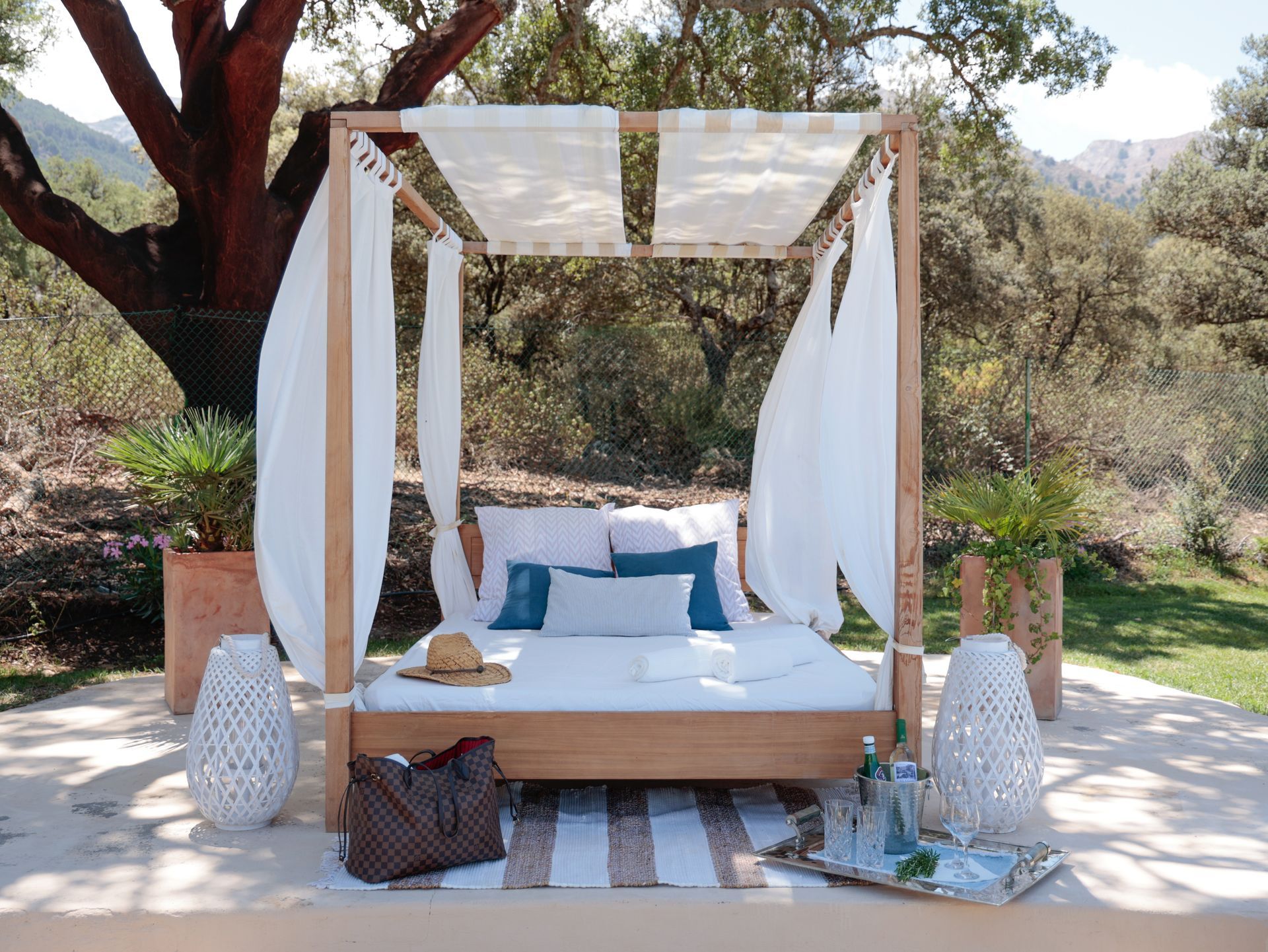 Canopy daybed with white curtains under old cork oak trees