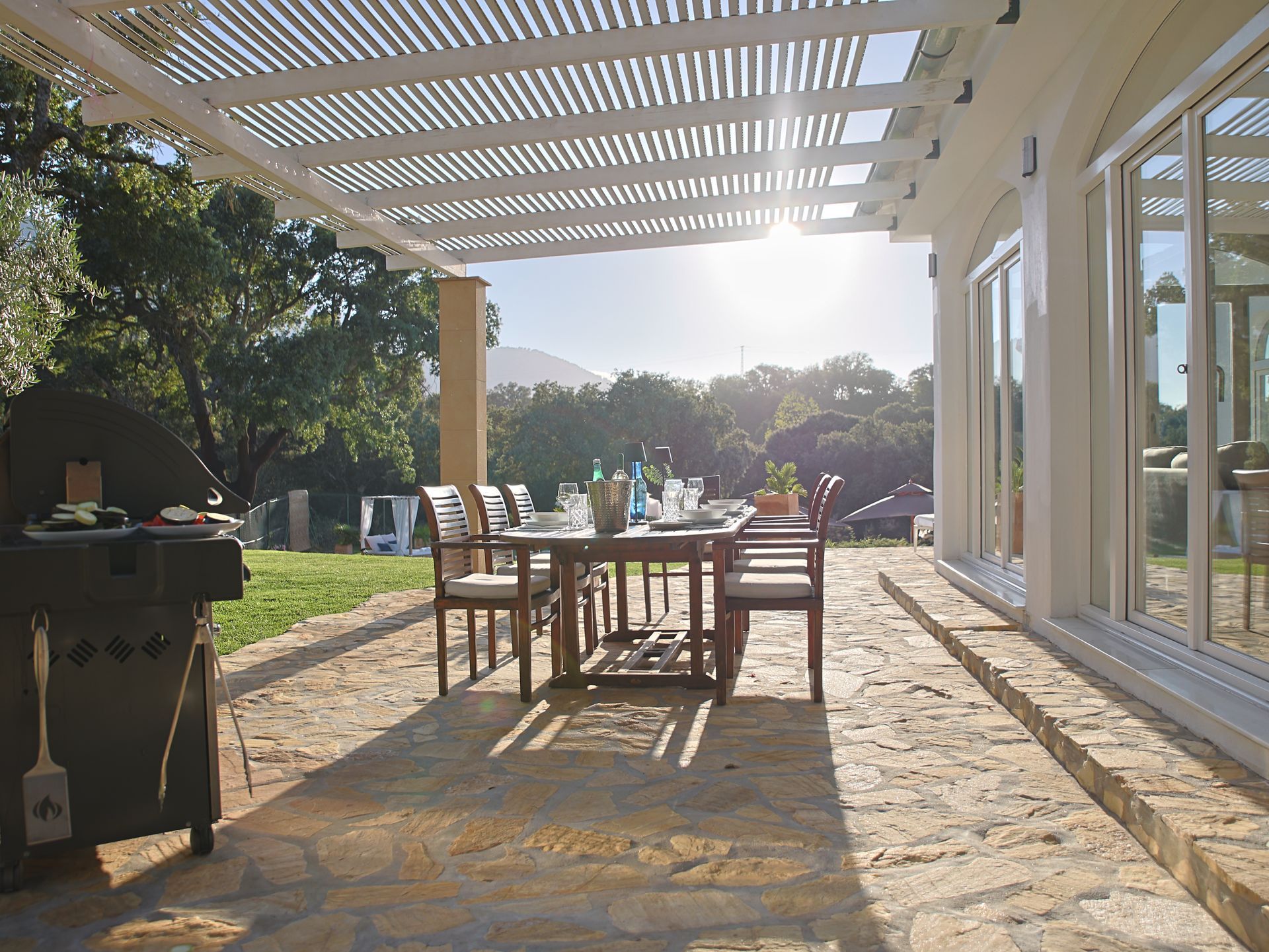 Outdoor dining table under the pergola with gas grill and garden view