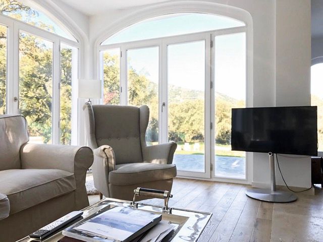 Cosy armchairs and TV in front of floor-to-ceiling windows with garden view