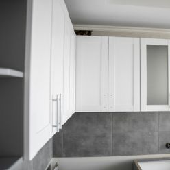 Una cocina con gabinetes blancos y una pared de azulejos grises.