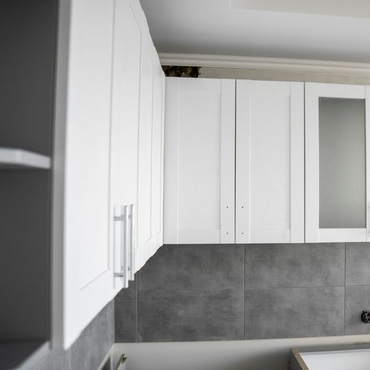 Una cocina con gabinetes blancos y azulejos grises.