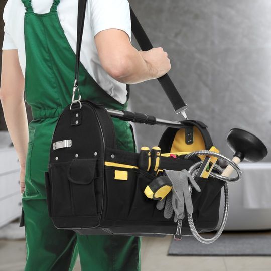 Un hombre con un mono verde lleva una bolsa llena de herramientas.