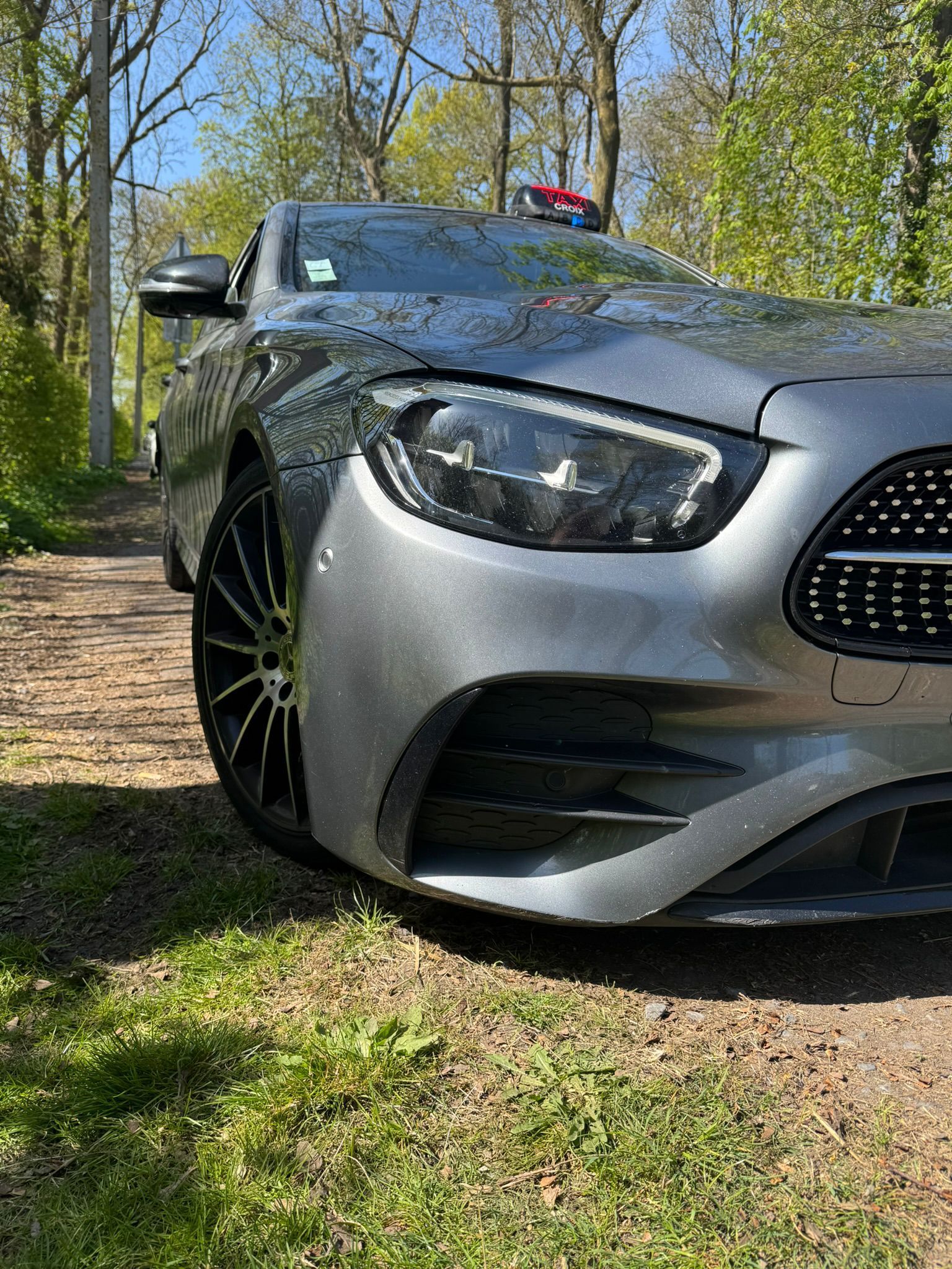 Une Mercedes-Benz gris foncé garée sur un chemin de terre entouré d'arbres par une journée ensoleillée.