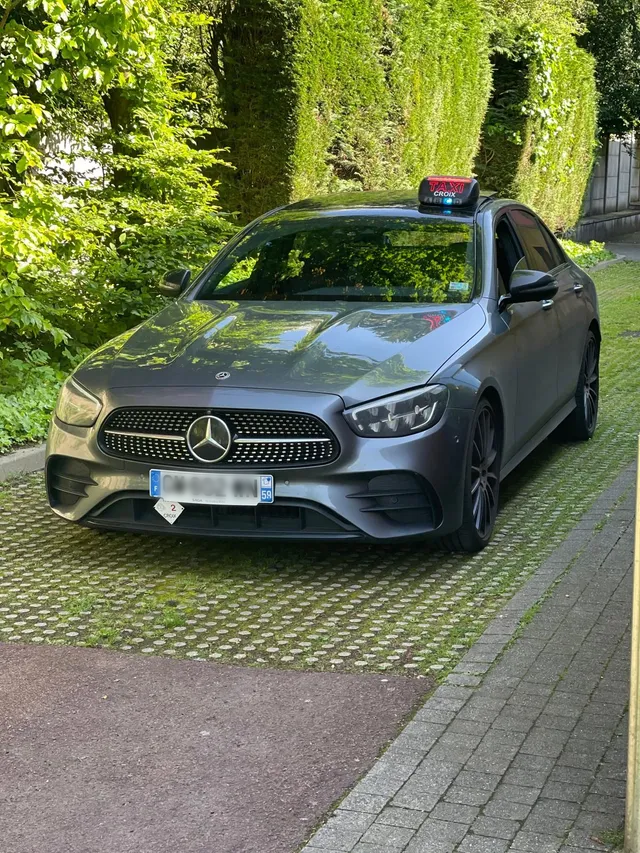 Une berline Mercedes grise avec un gyrophare sur le toit est garée sur une allée pavée entourée d'une végétation luxuriante.