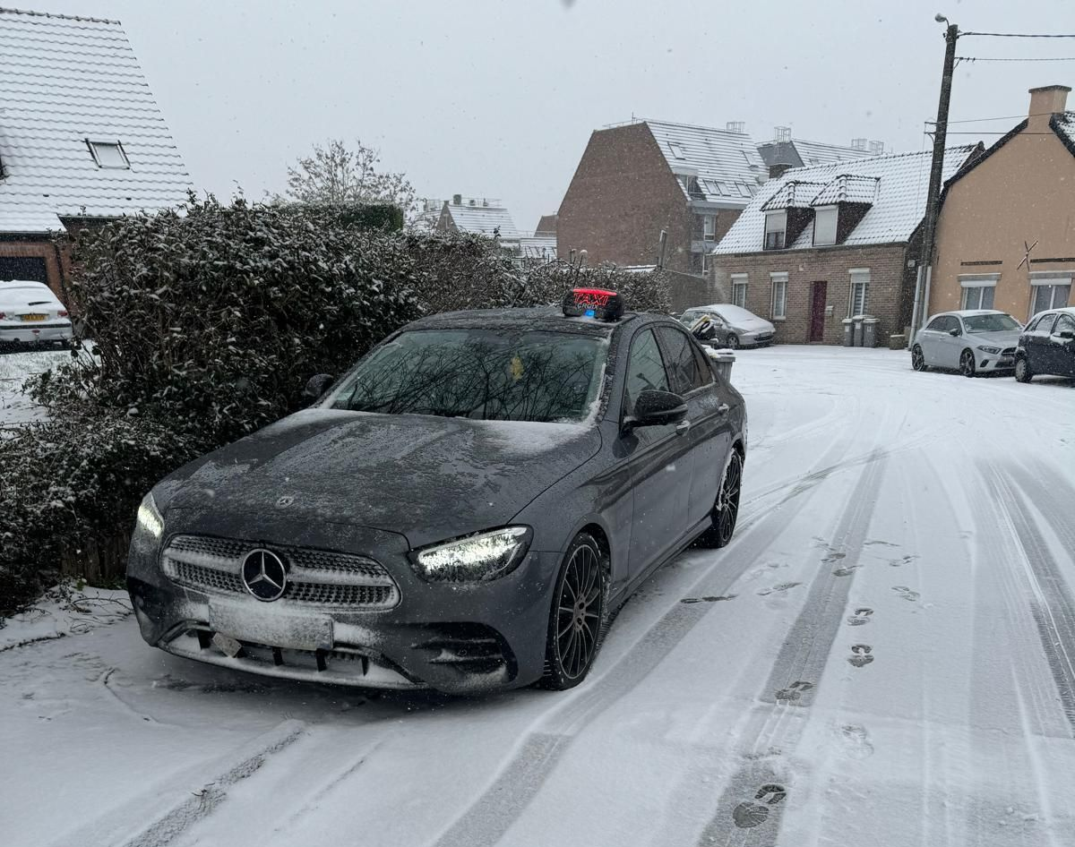 Une berline Mercedes-Benz grise garée dans une rue enneigée d'un quartier résidentiel.
