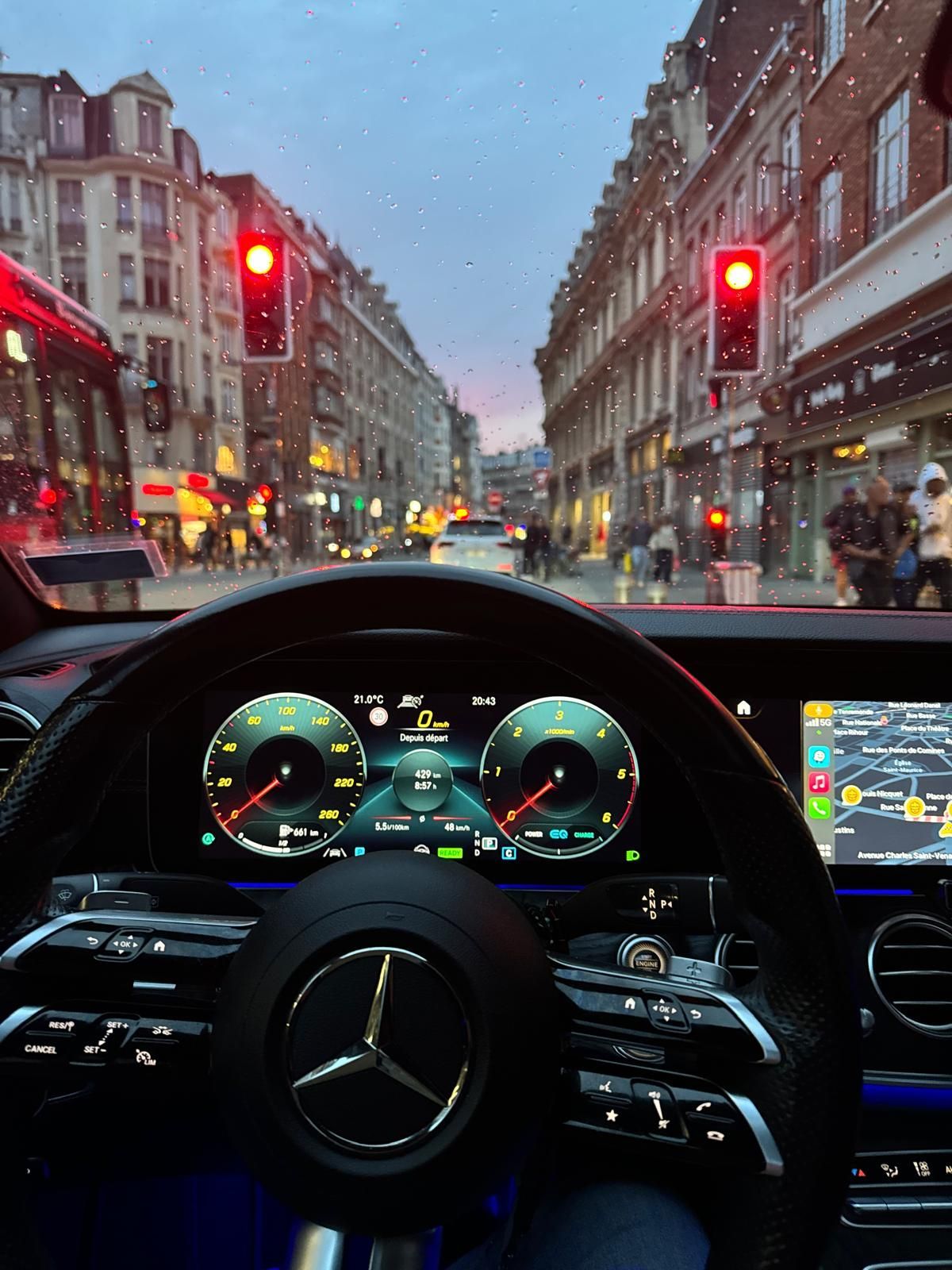 Vue depuis le siège conducteur d'une Mercedes-Benz, arrêtée à un feu rouge dans une rue de la ville au crépuscule.