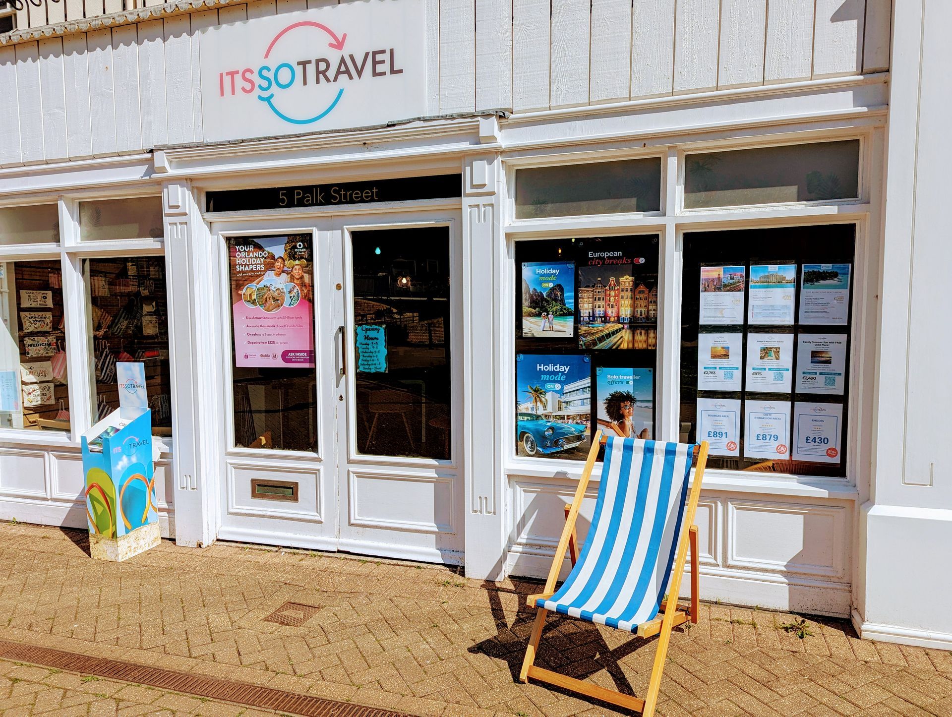 A blue and white striped beach chair is sitting in front of a travel agency.