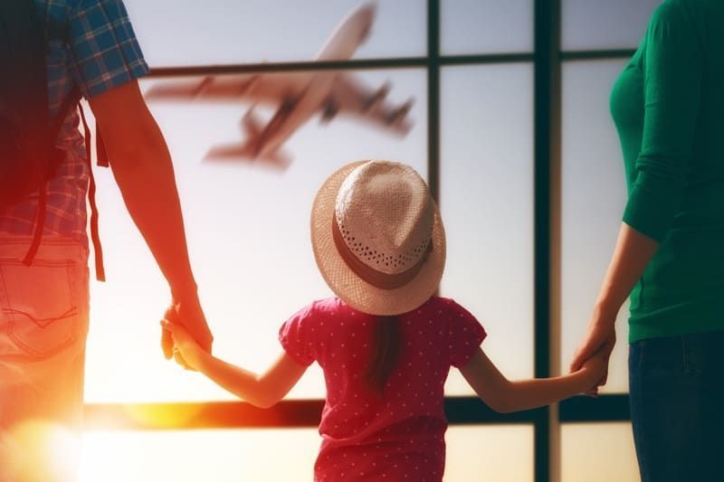 A family is holding hands and looking out a window at an airplane.