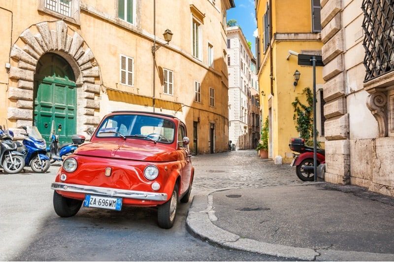 A red car is parked on the side of a narrow street.
