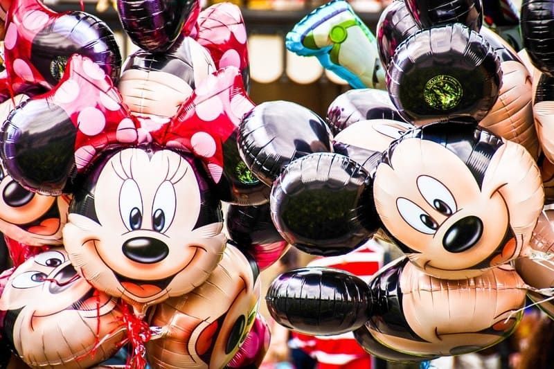 A bunch of mickey mouse and minnie mouse balloons hanging from a string.