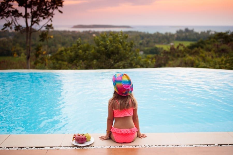 A little girl is sitting on the edge of an infinity pool.