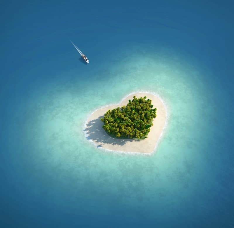 A heart shaped island in the middle of the ocean with a boat in the background.