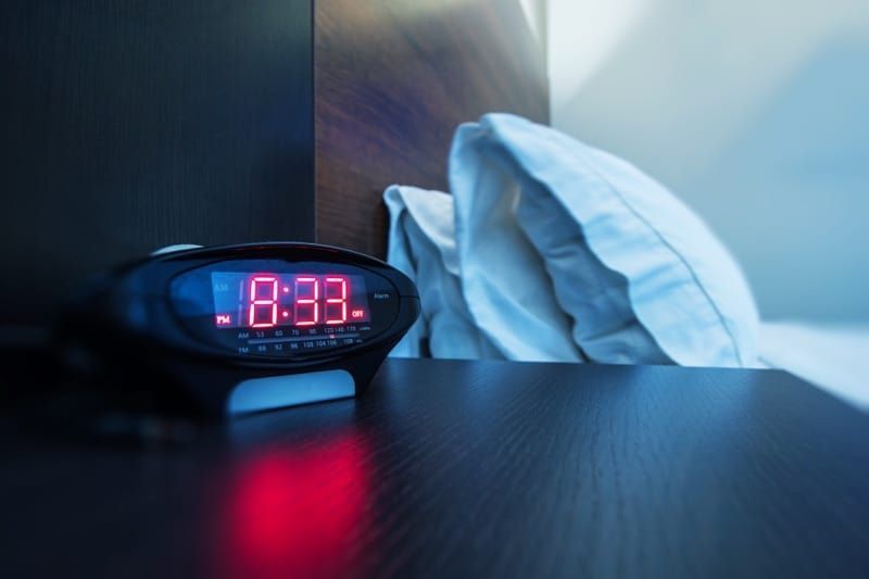 An alarm clock is sitting on a nightstand next to a bed.