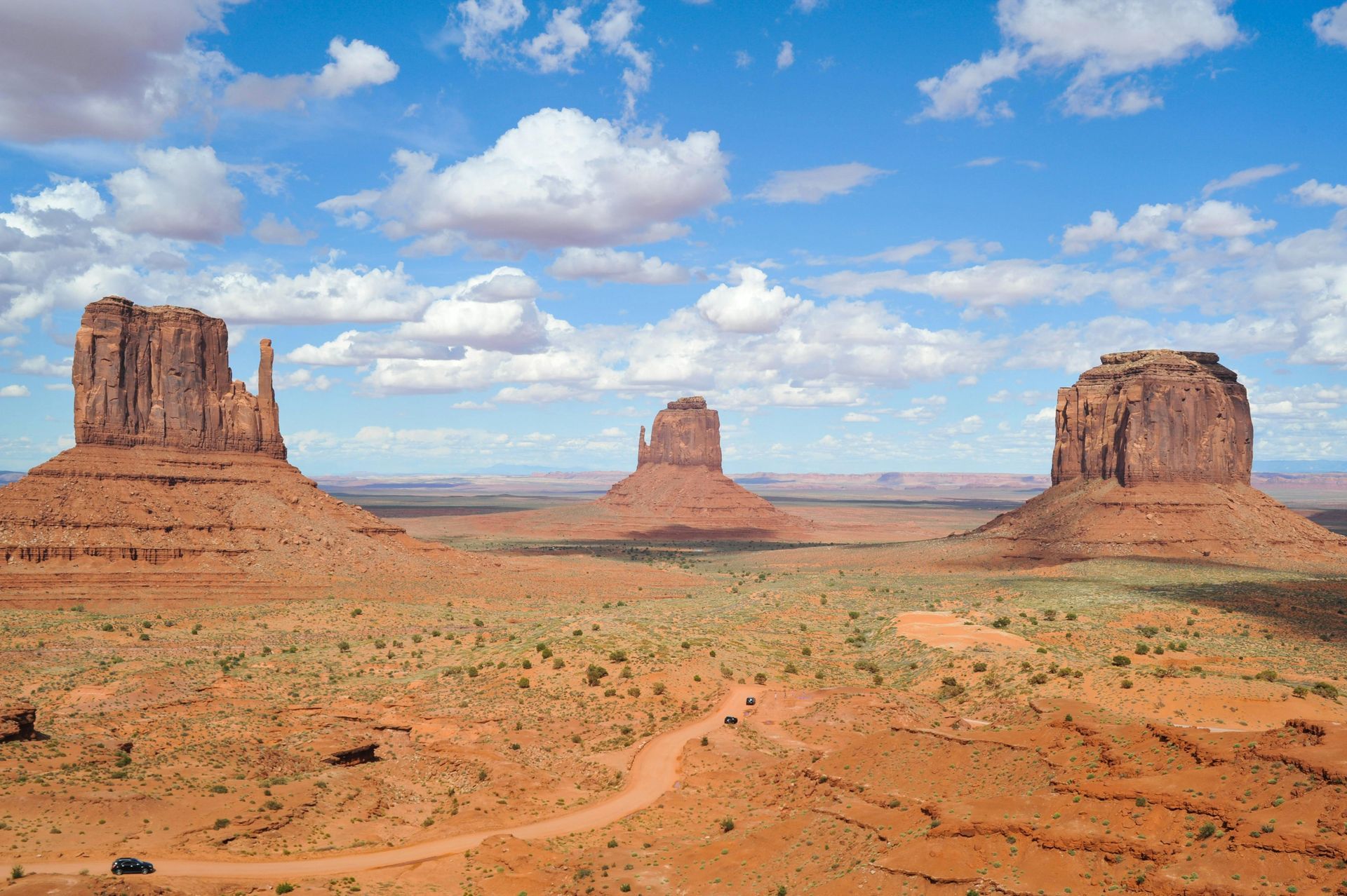 Sandstone buttes rise from desert floor under a blue sky with clouds; Monument Valley, Utah.