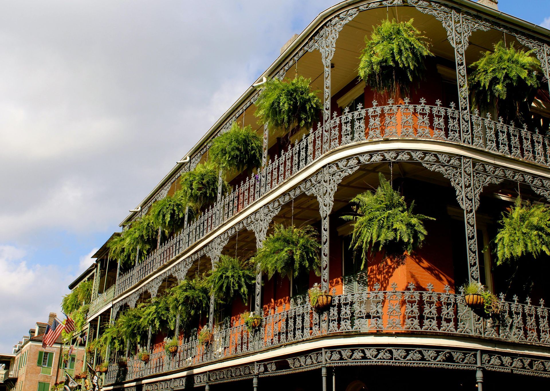 Ornate balconies of a New Orleans building, adorned with ferns, against a cloudy sky.