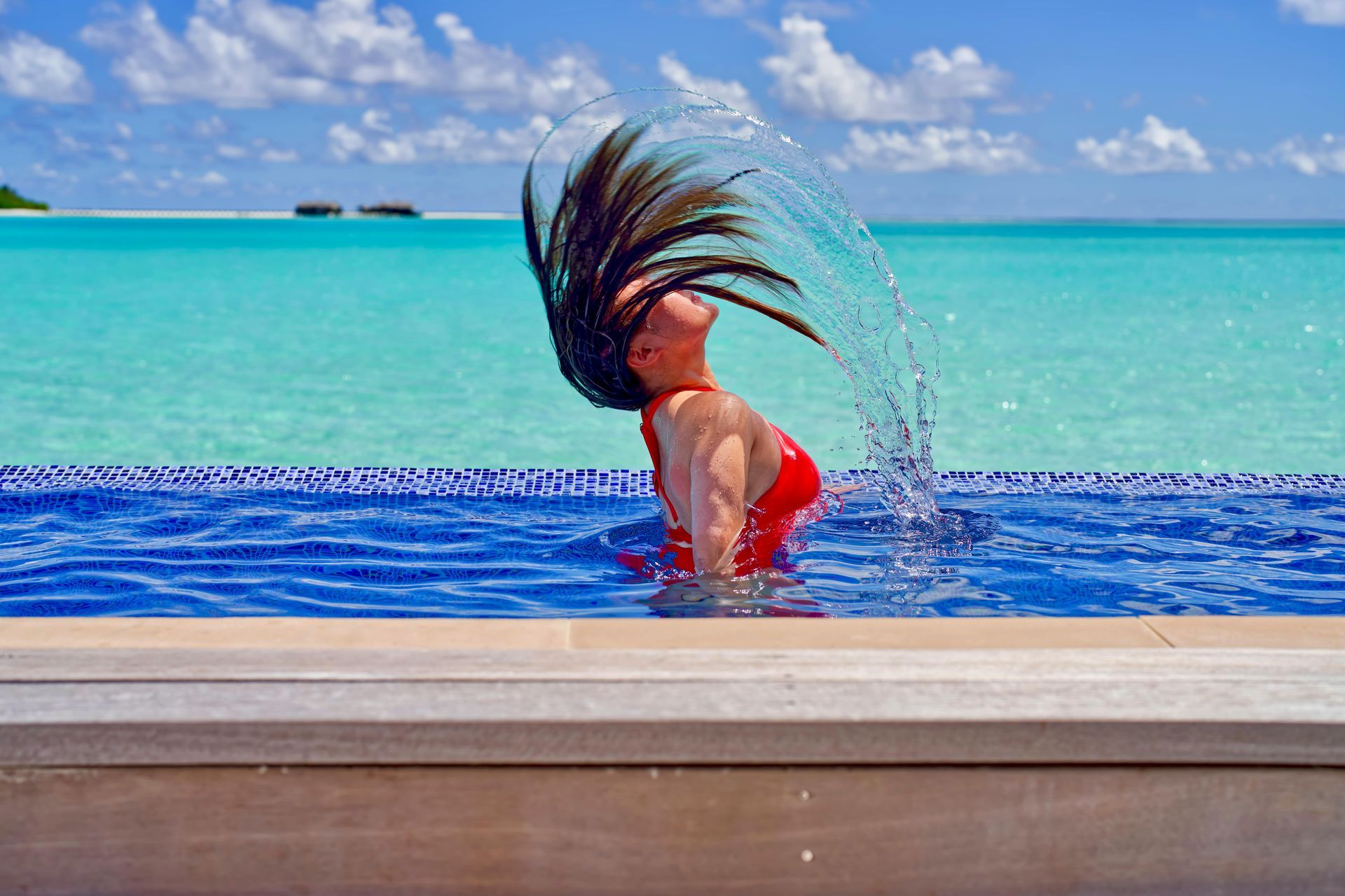 A woman in a red bikini is splashing her hair in a swimming pool.