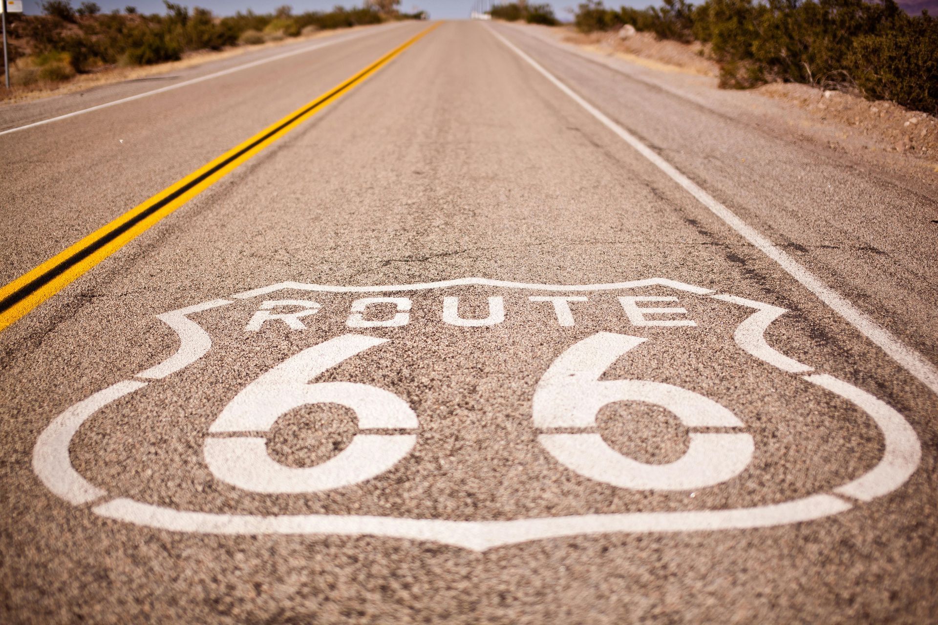 Route 66 sign painted on asphalt road, part of a California road trip