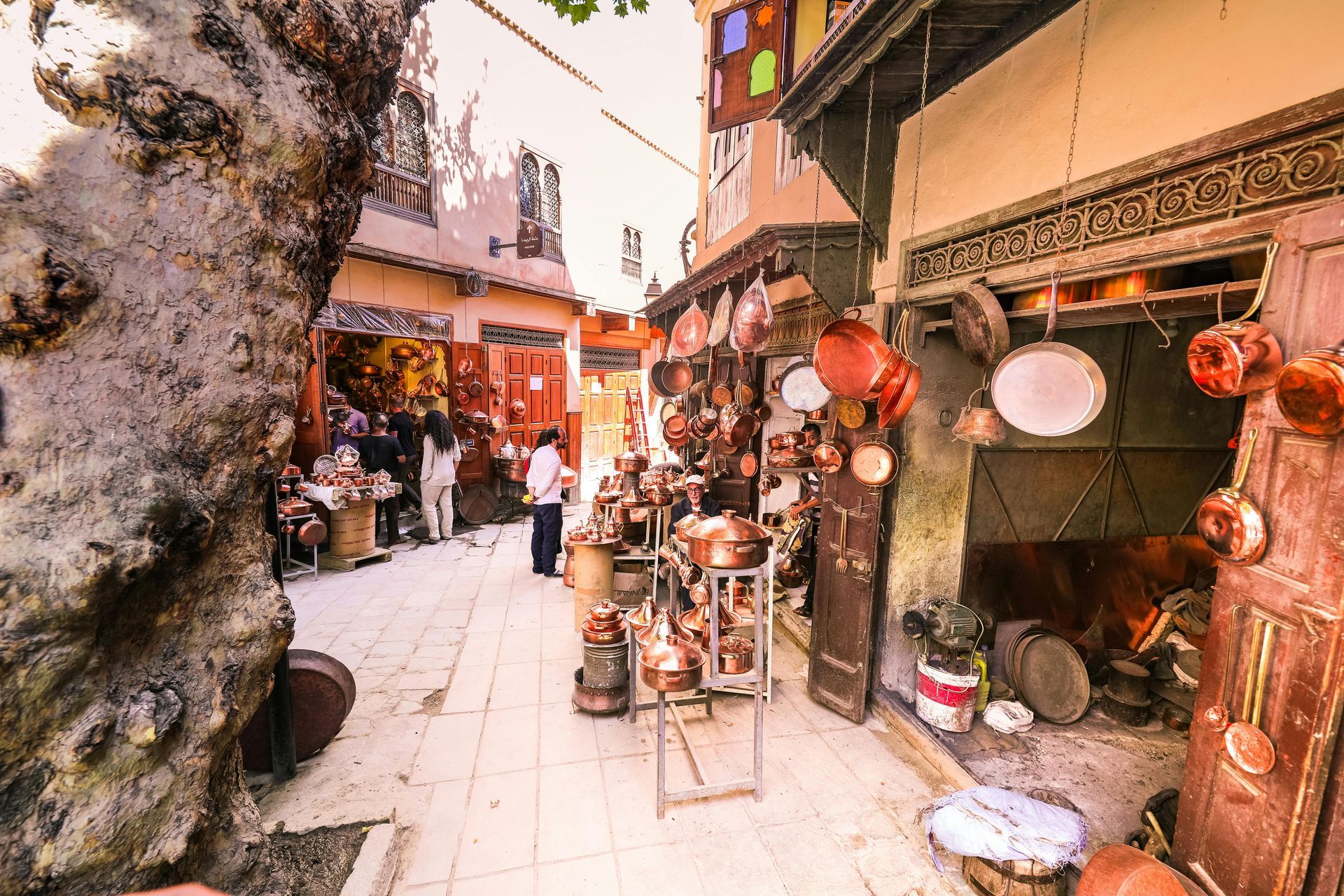Narrow alley in a Moroccan souk, lined with copper cookware and shops, people browsing.