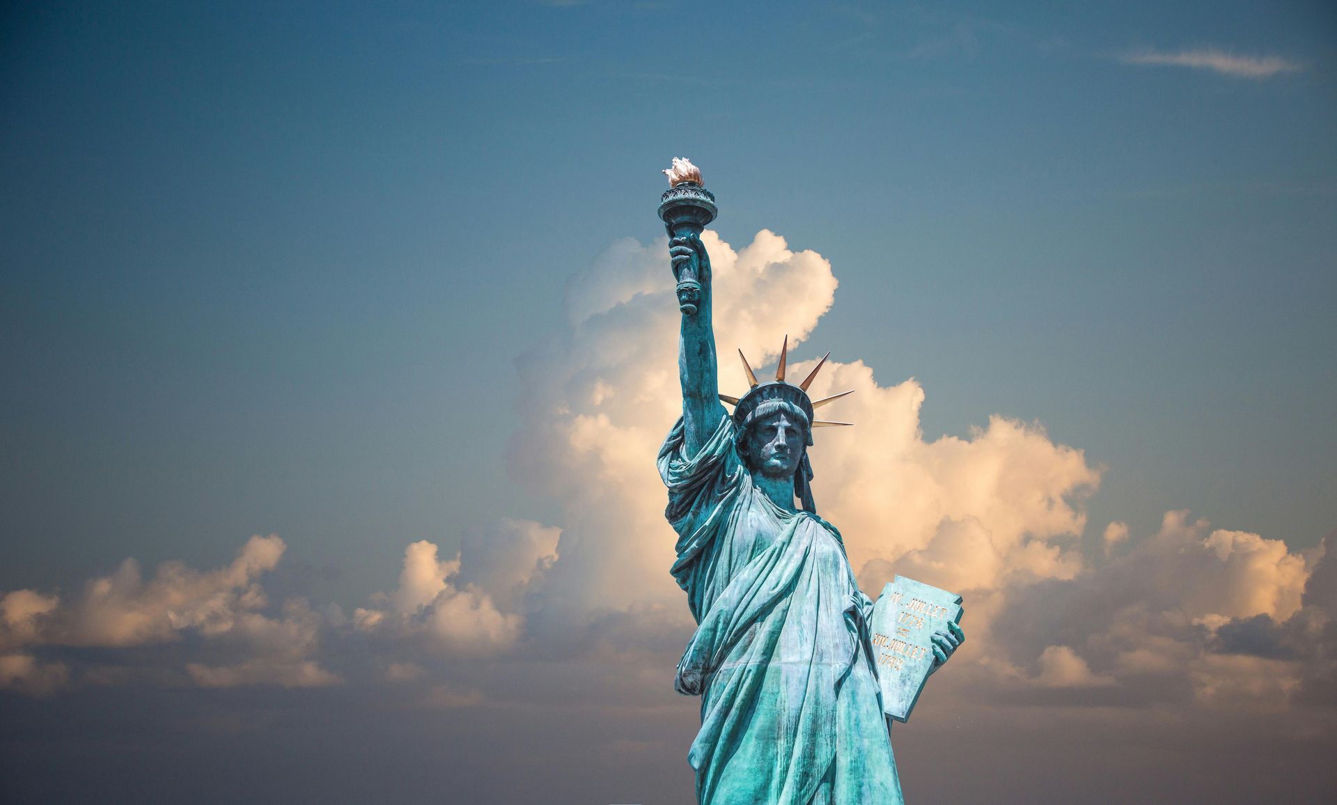 The statue of liberty is standing in front of a cloudy sky.