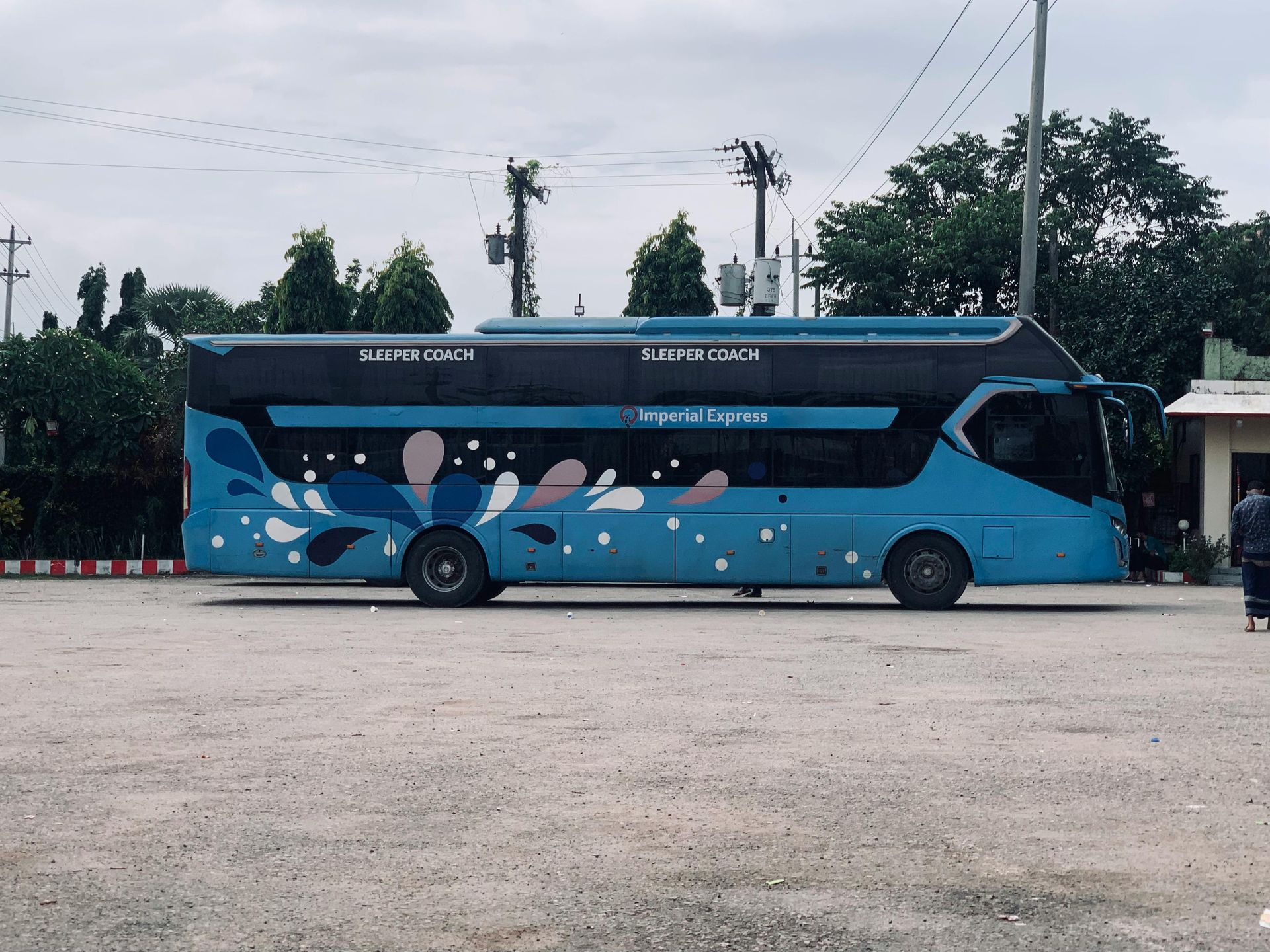 Blue double-decker sleeping coach bus parked in a lot with decorative floral design.