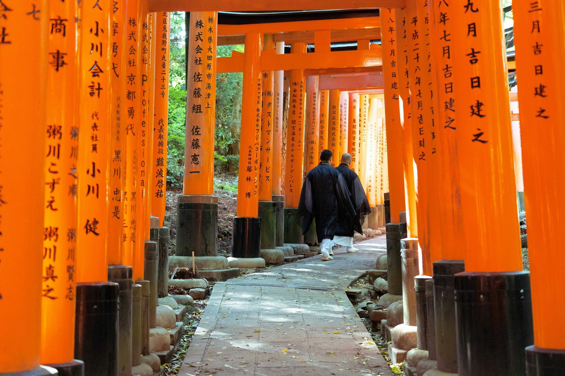 Two figures walk through orange torii gates in Japan.