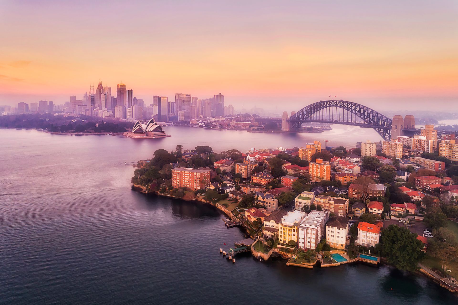 Sydney Harbour at sunrise with city skyline, bridge, and opera house.