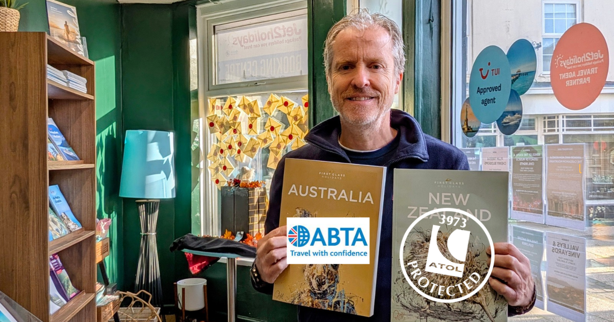 Man in travel agency holding up brochures with ATL and ABTA logo's on.