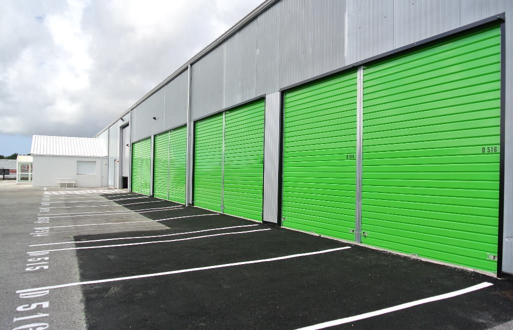 Vue extérieure d'un entrepôt avec des portes sectionnelles métalliques vertes et de l'asphalte noir.
