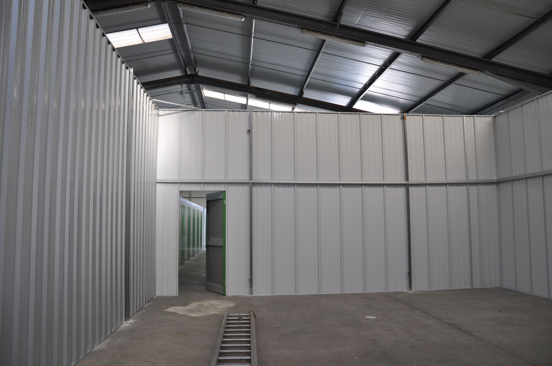 Des conteneurs de stockage en tôle ondulée blanche avec une porte verte ouverte. À l'intérieur, on aperçoit un autre conteneur.