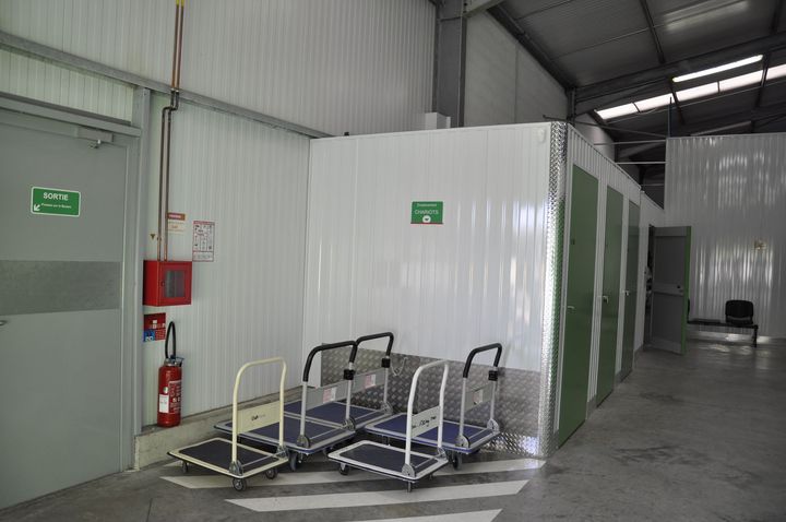 Unités de stockage avec portes sectionnelles vertes et parois en tôle ondulée. Sol en béton. Finitions blanches.