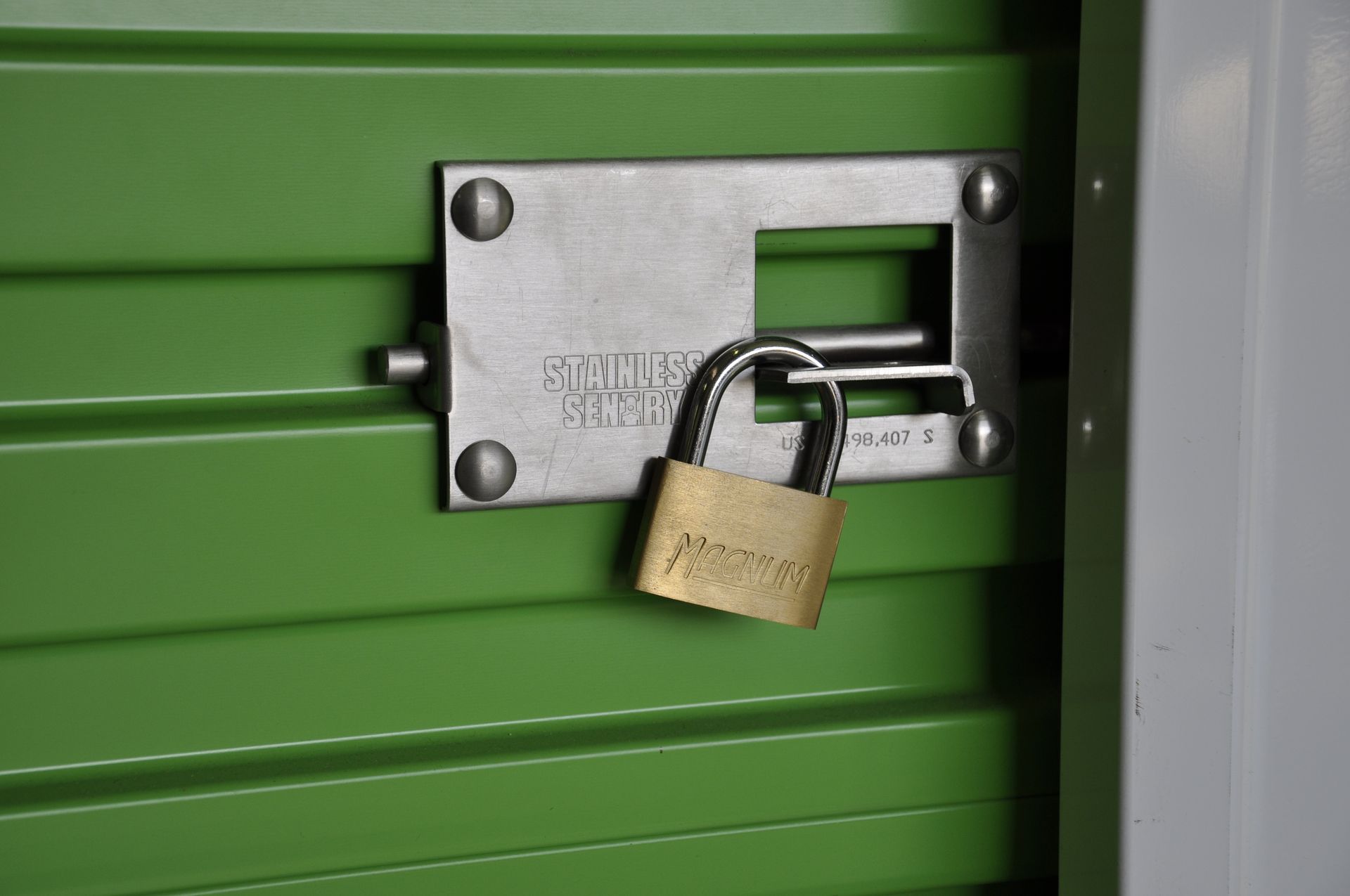 Porte de box de stockage verte sécurisée par un loquet métallique et un cadenas doré.
