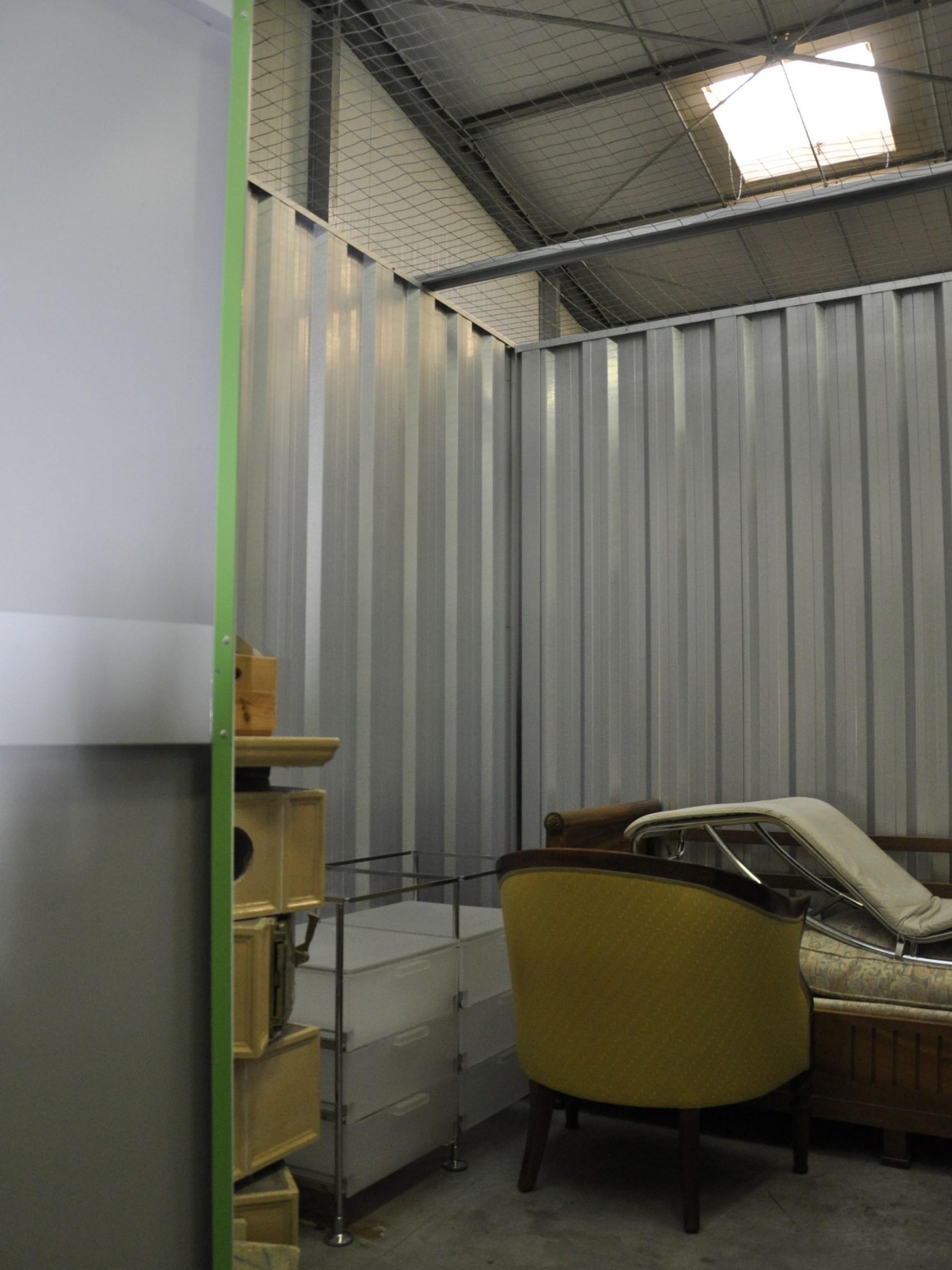 Unités de stockage avec portes sectionnelles vertes, extérieur en métal blanc et gris. Sol intérieur en béton.